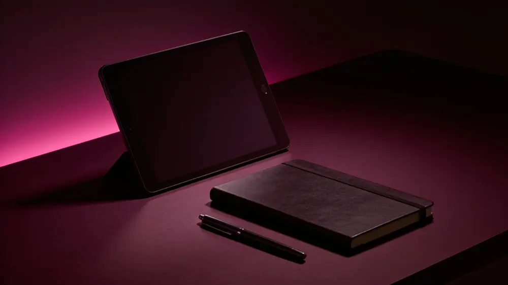 A dimly lit desk with a tablet, a notebook and a pen — the working set-up behind this review